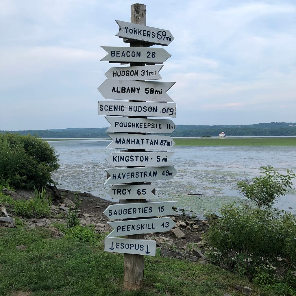 image description: signpost with arrows to NY cities pointing in different directions with distances: Yonkers, Beacon, Hudson, Albany, Scenic Hudson, Poughkeepsie, Manhattan, Kingston, Haverstraw, Troy, Saugerties, Peekskill, Esopus