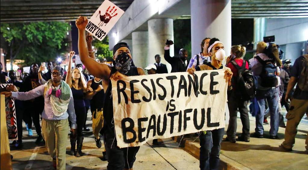 masked folks carrying a banner that says "Resistance Is Beautiful.